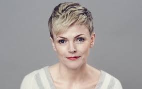 Person with short hair wearing a light-colored top against a gray background